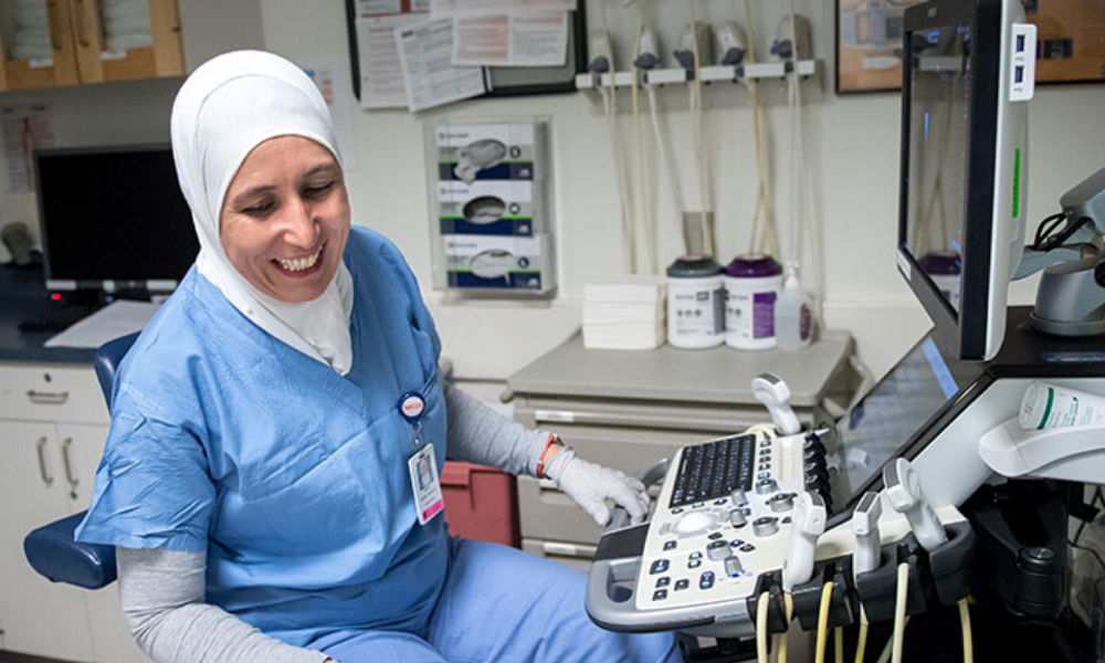 An ultrasound technologist talks with a patient on an exam table